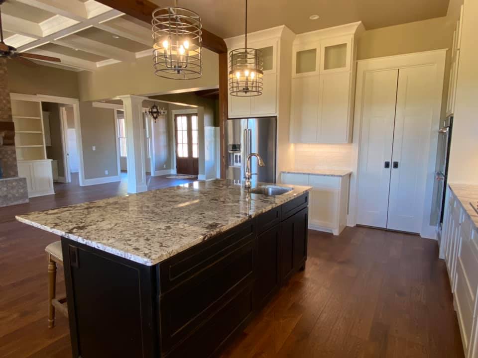 Photo of massive kitchen island with custom drop light fixtures, loads of built in cabinets, hardwood flooring and custom cabinets in dining space