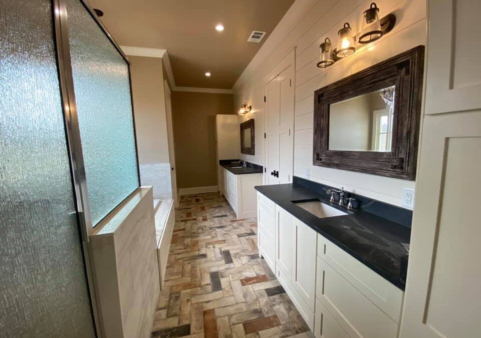 Photo of master bath in home with soaker tub separate shower and separate his/her sinks. countertops are black marble and herringbone tile flooring