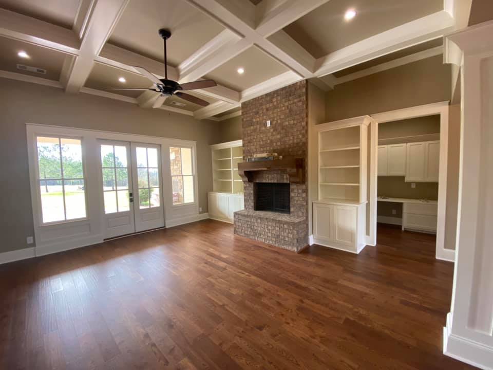 wide view photo of great room in The Boone House in Oconee, GA, with brick fireplace, channeled ceiling, hardwood floors and dual built in book cases