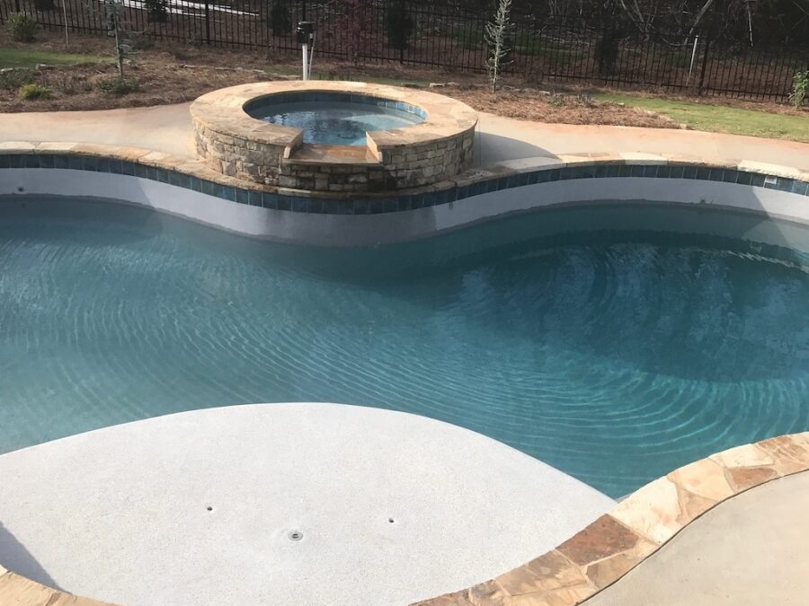 Photo of swimming pool with stone framed hot tub with water spill to pool