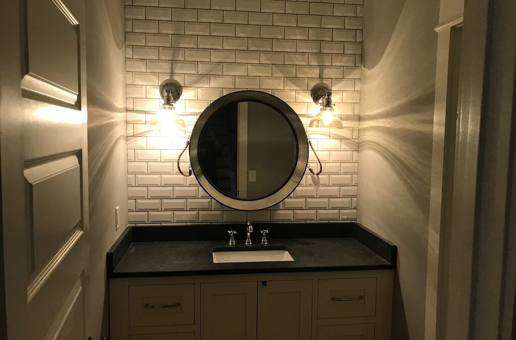 Photo of bathroom sink area with round mirror and subway tile back wall